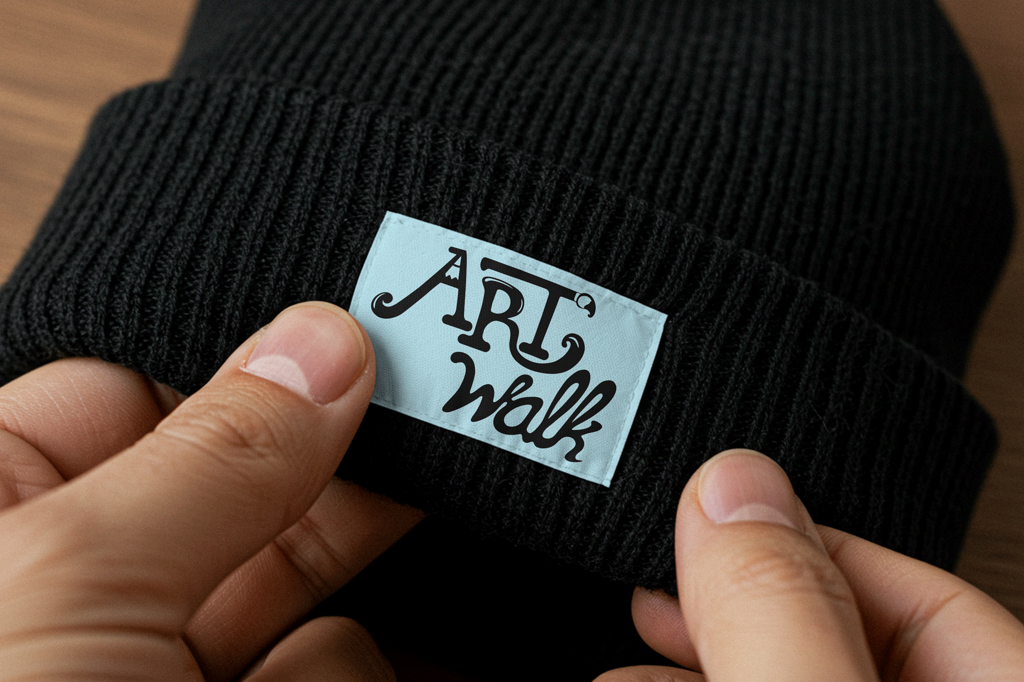 a black knit beanie with the ArtWalk stacked logo in black on a light blue decorative tag on the front