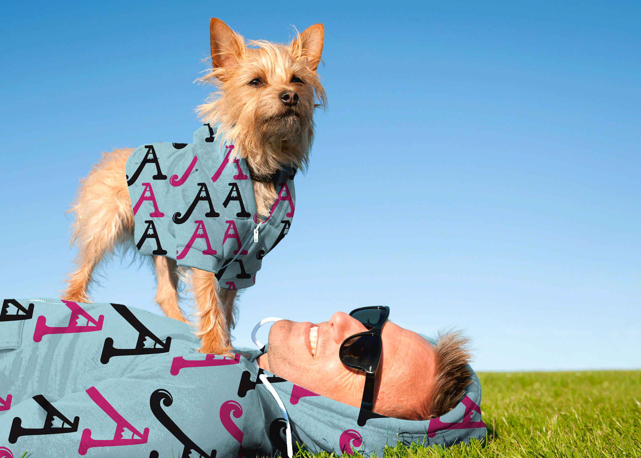 a man and his dog laying in the grass, both wearing pink and light blue ArtWalk sweatshirts